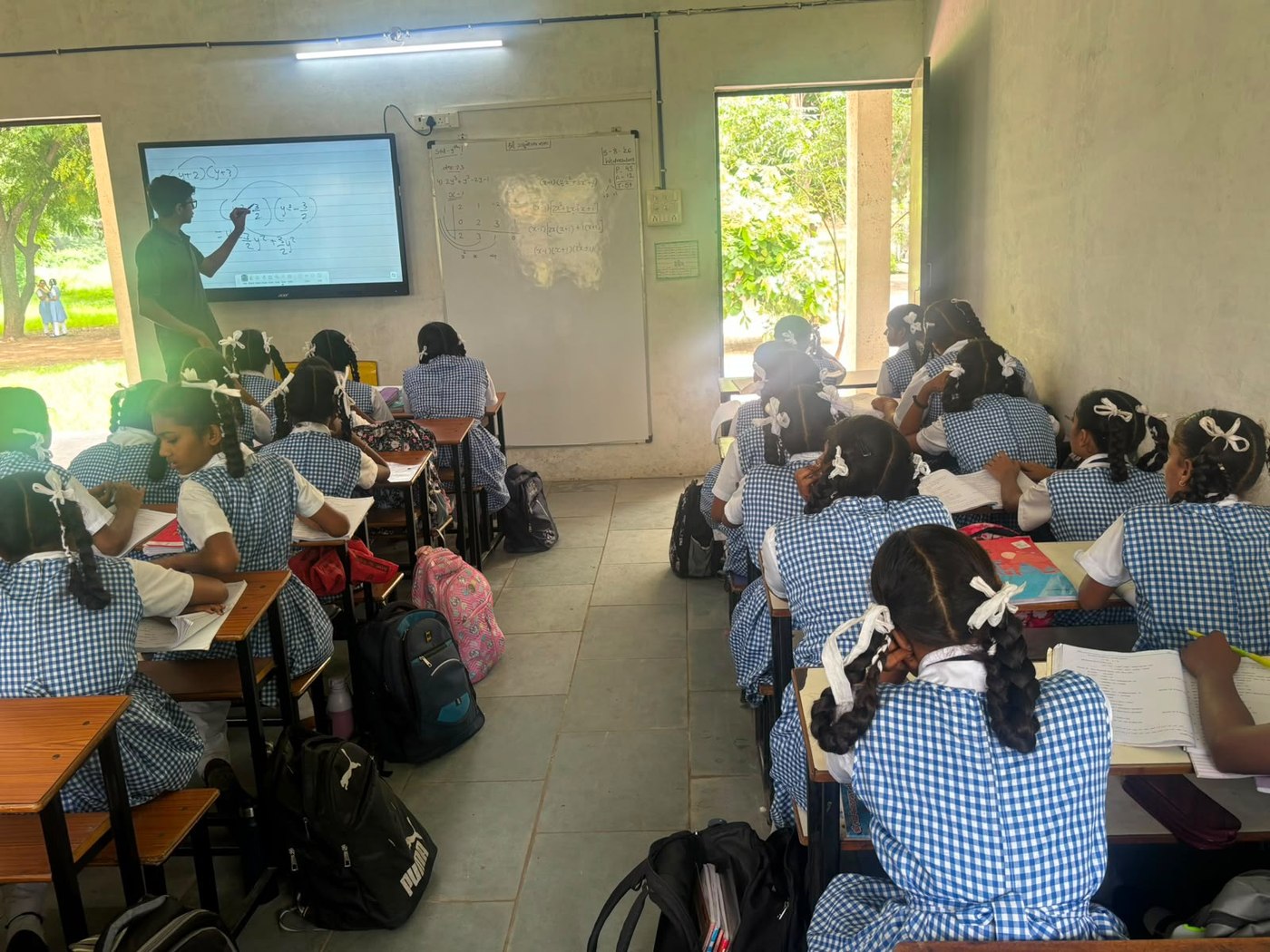 Rishabh writing an equation on the smart board, students seated at desks in the foreground